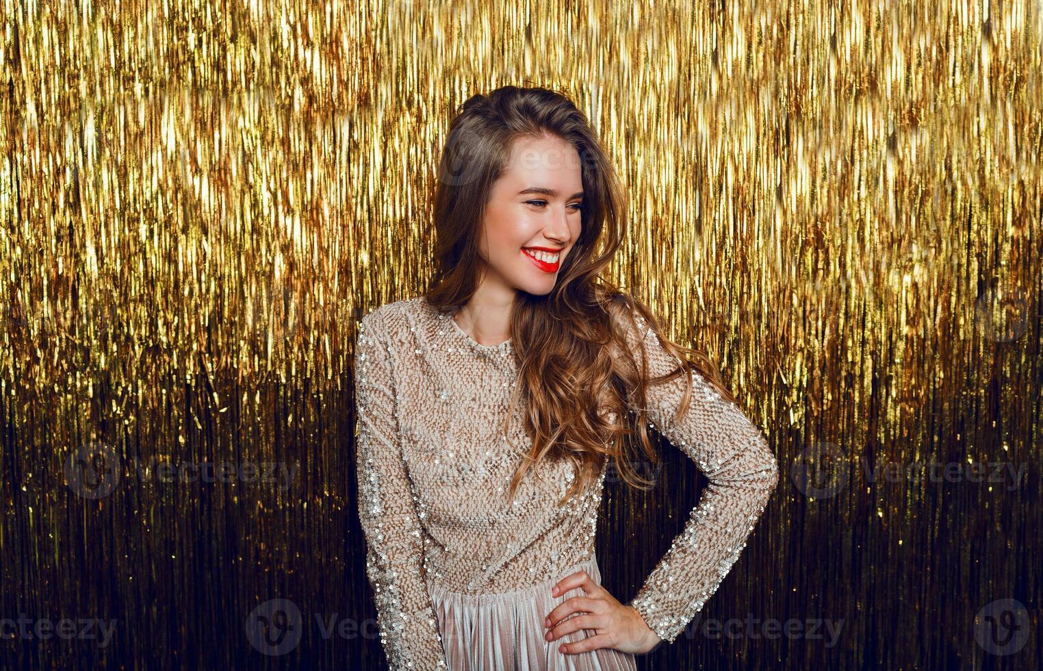 Elegant celebrating woman with surprise  face standing  over  golden sparkling  background. Red lips. New year party. photo