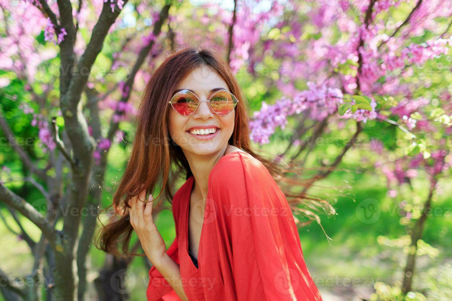 Carefree girl in stylish straw hat and coral dress enjoying  spring day in sunny garden  on blooming tree background. photo