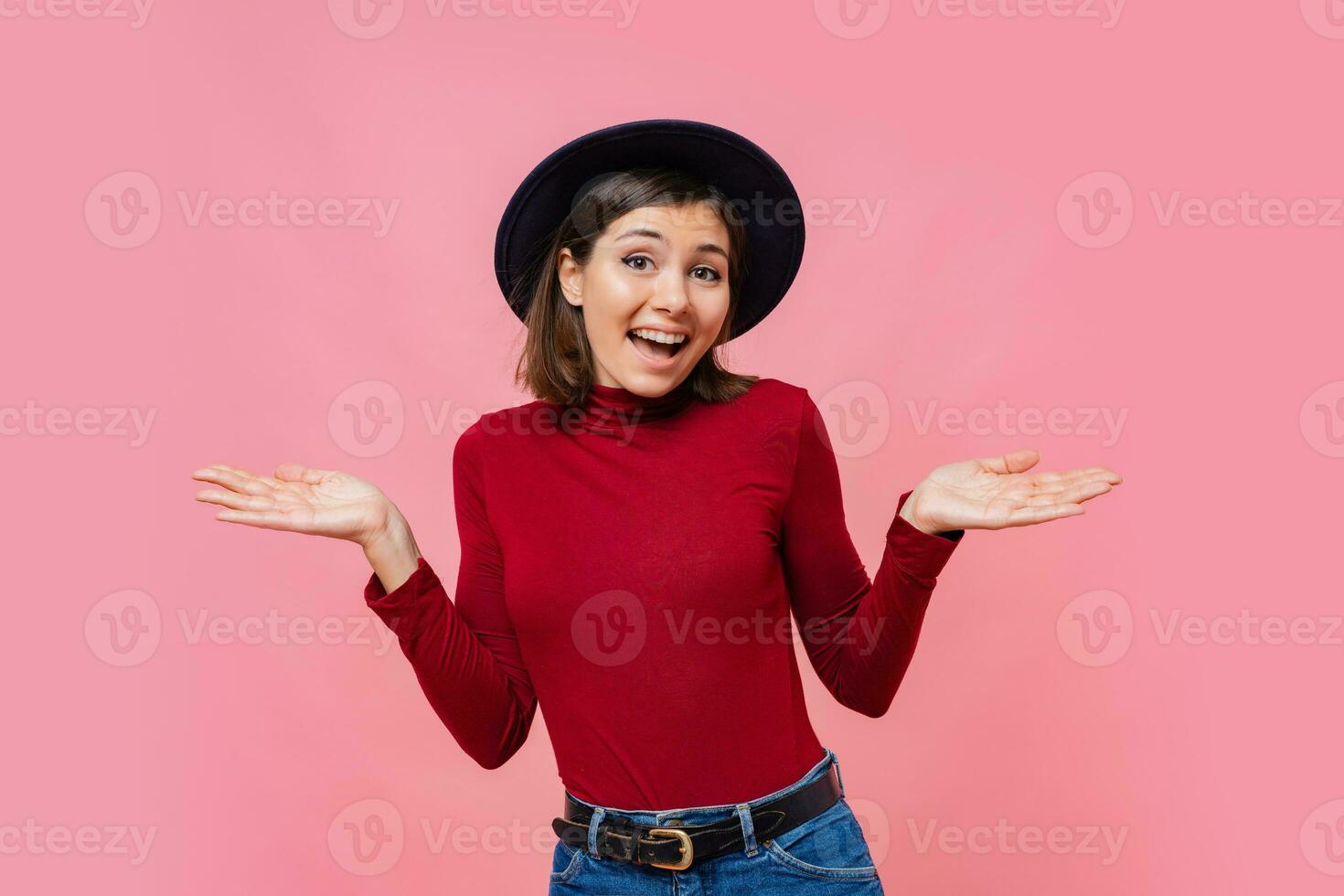 Puzzled  cute  female  spreads hands with doubt, dressed in  red  jumper, isolated over  pink background, blank copy space. Woman faces dilemma, being unsure photo