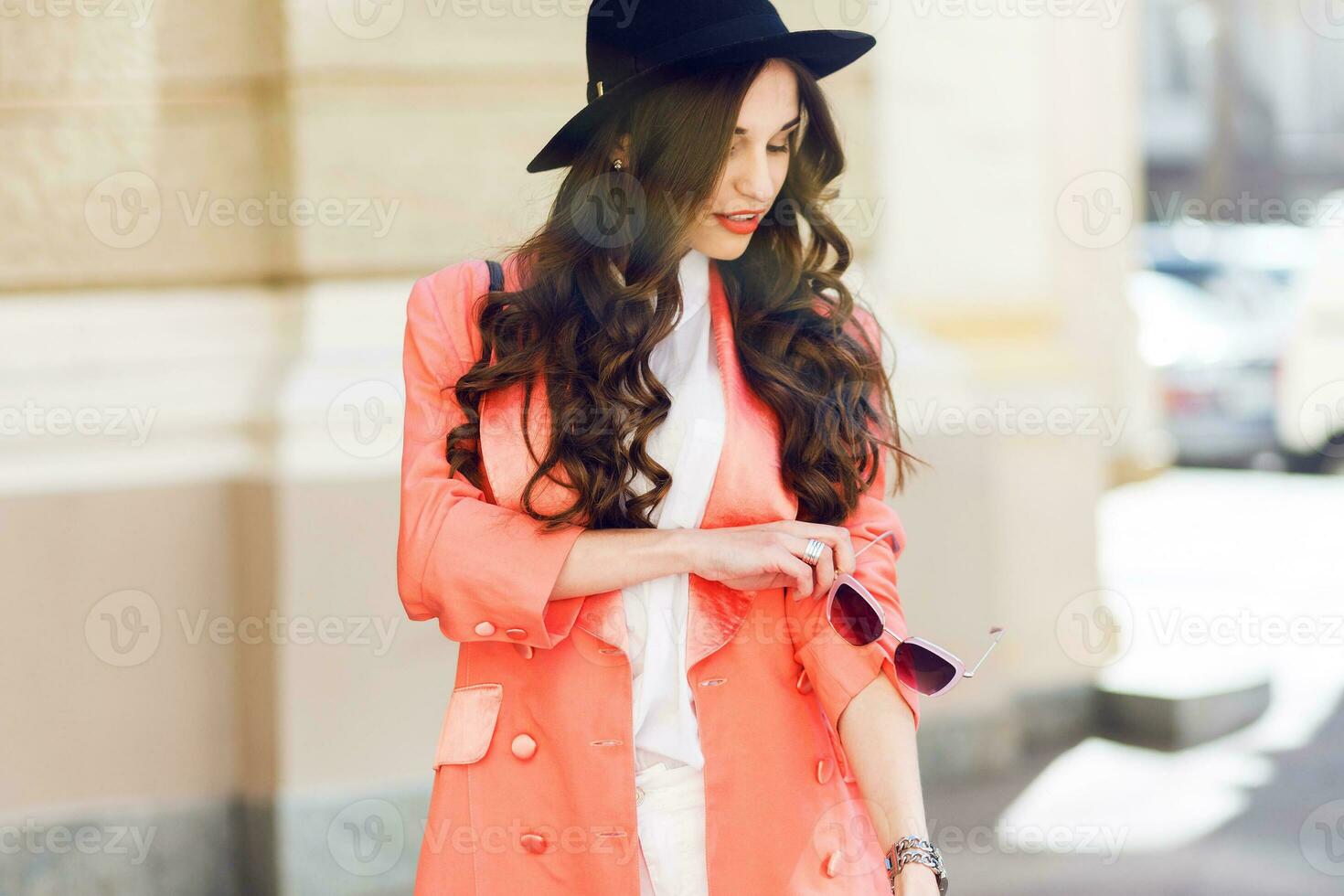 al aire libre cerca arriba Moda retrato de sexy elegante casual mujer en negro sombrero, rosado traje , blanco blusa posando en antiguo calle antecedentes. primavera , otoño soleado día. ondulado peinado. foto