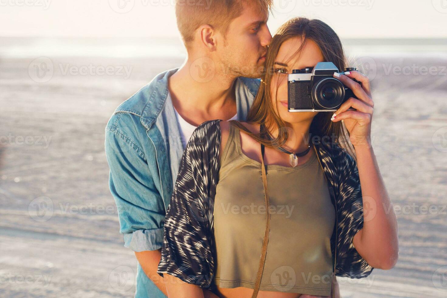 Couple in love posing on the evening beach, Young  hipster girl  and her handsome boyfriend taking photos with retro film camera. Sunset warm light.