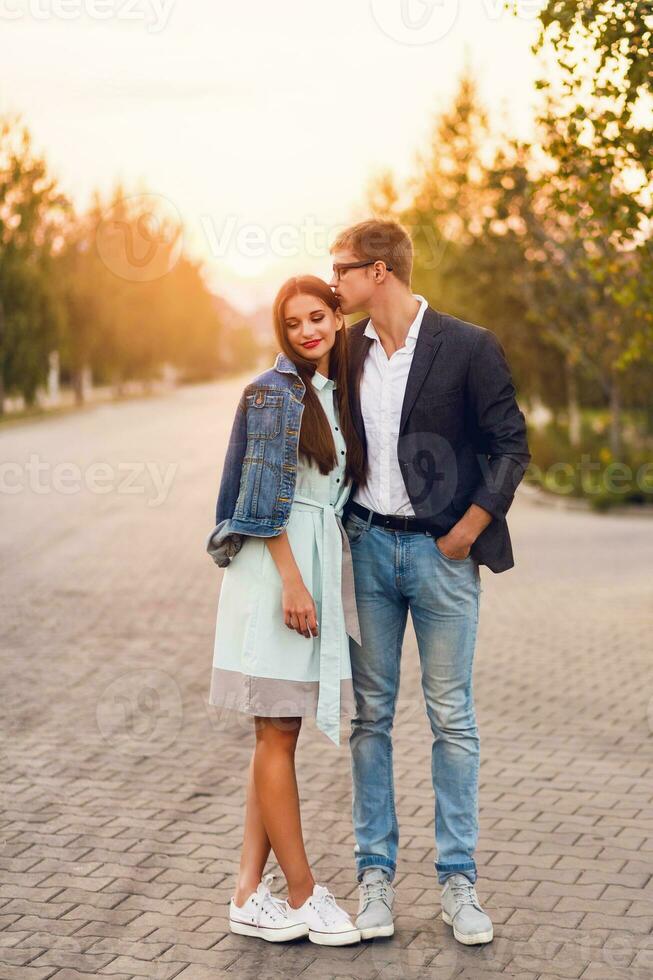 joven hipster Pareja en amor exterior. maravilloso sensual retrato de joven elegante Moda Pareja posando en verano puesta de sol . bonito joven niña en pantalones chaqueta y su hermoso novio caminando . foto