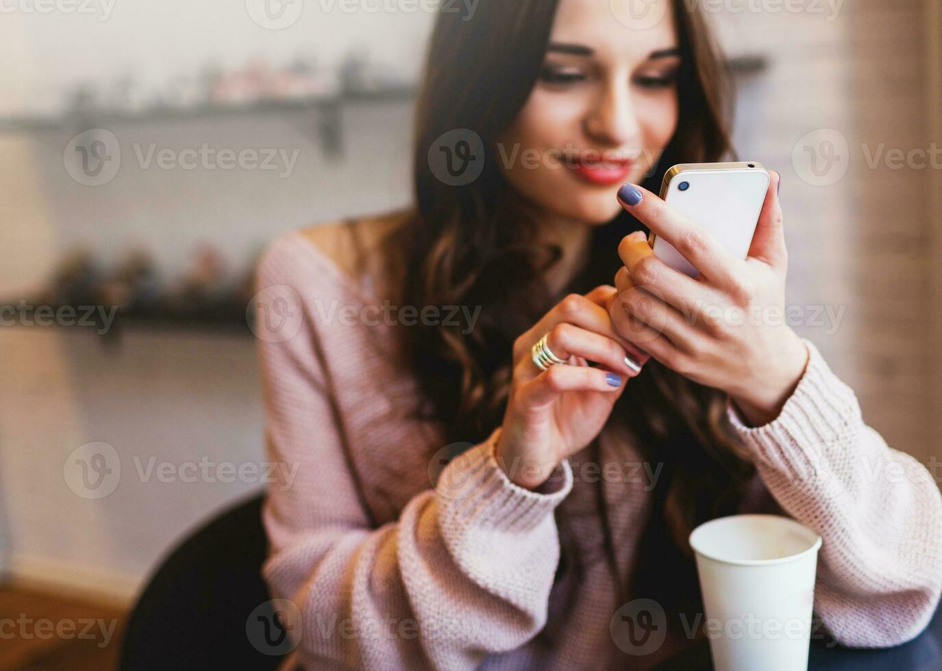 Woman typing write  message on smart phone in a  modern cafe. Cropped image of young  pretty girl sitting at a table with  coffee or cappuccino  using mobile phone. photo