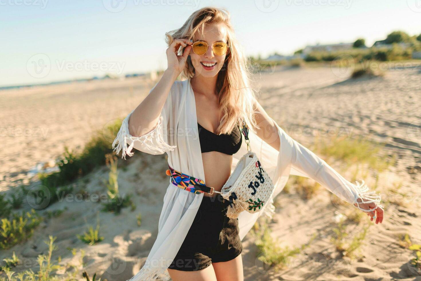 Graceful blonde girl on trendy boho beach cover with fringe and accessories on amazing lonely beach photo