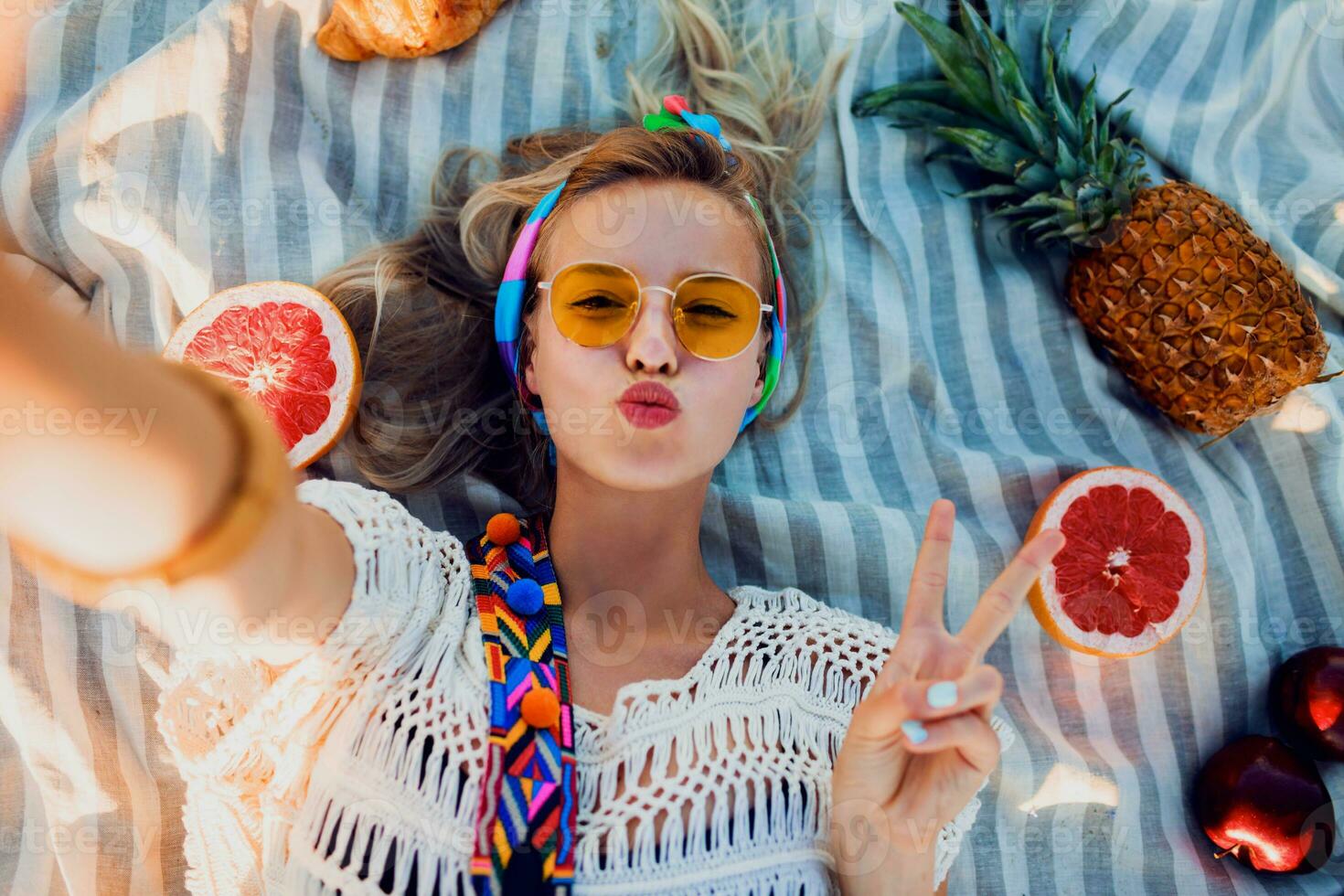 emocionado niña haciendo selfie en playa toalla. boho accesorios. amarillo gafas de sol.arriba vista. foto