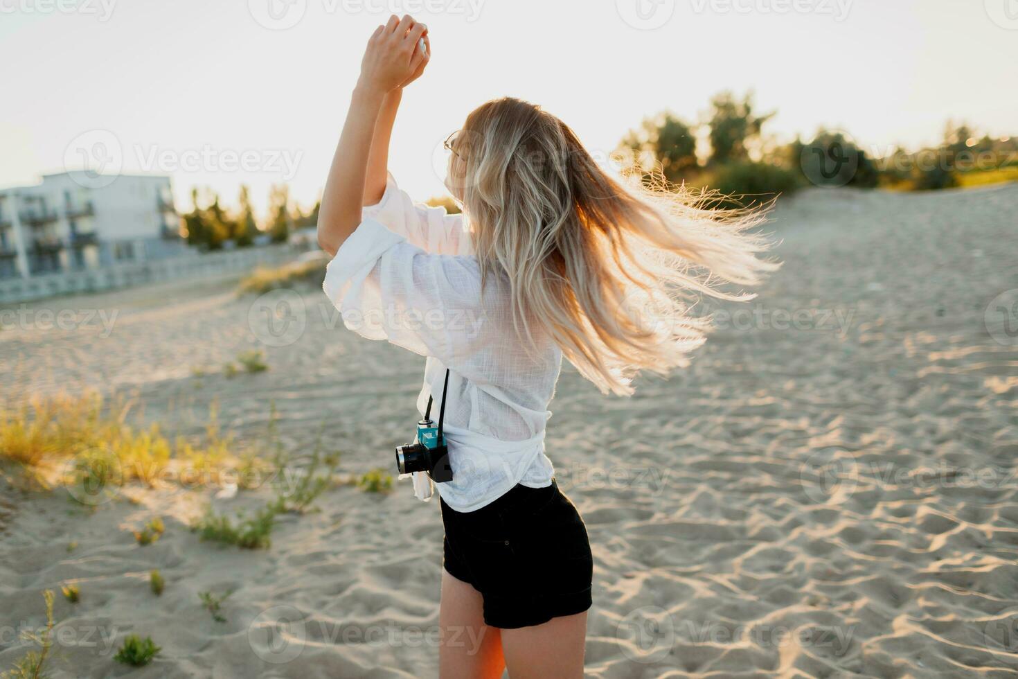 Stylish shapely girl with retro camera posing on sunny evening beach. Tropical mood. photo