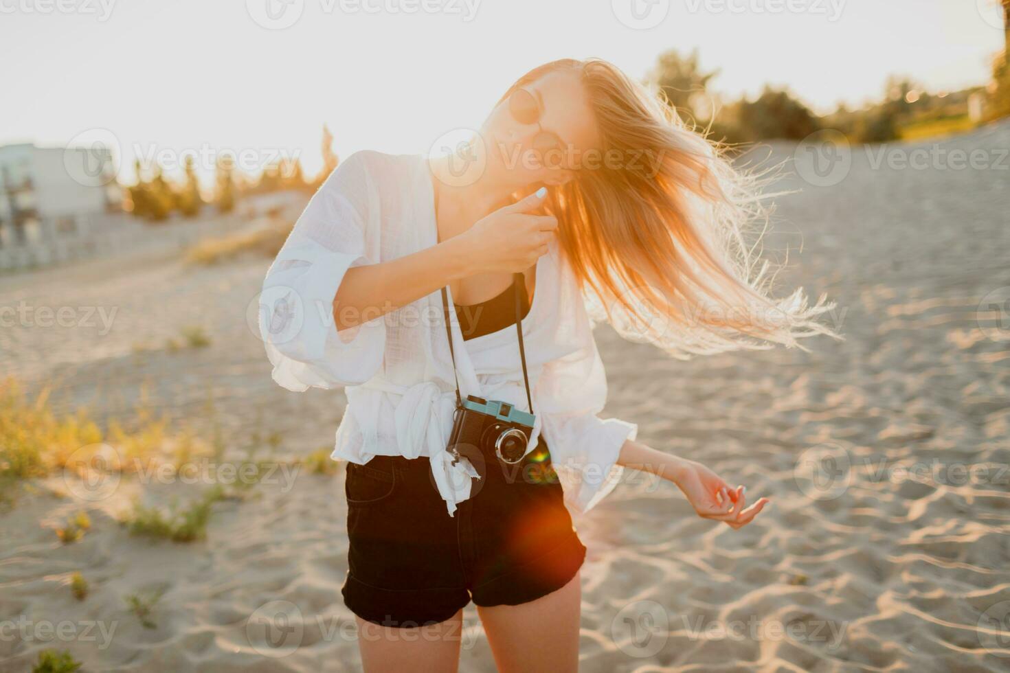 Stylish shapely girl with retro camera posing on sunny evening beach. Tropical mood. photo