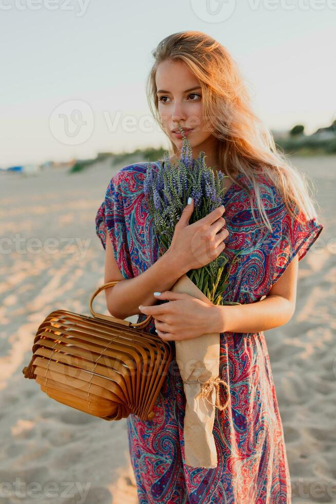 Summer image of romantic blonde woman in colorful dress walking on the beach with lavender. photo