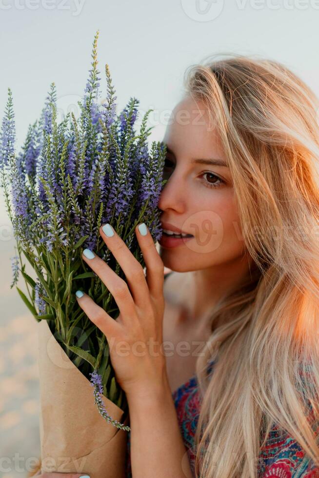 Beauty portrait of romantic blonde woman with bouquet of lavender looking at camera on the beach. photo