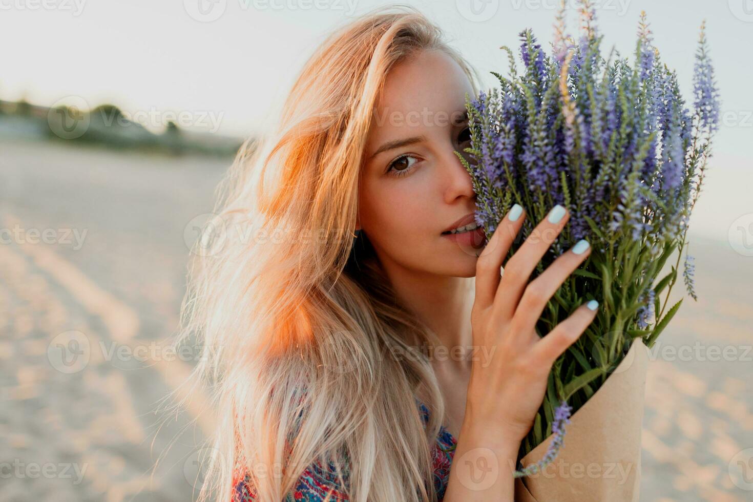 Beauty portrait of romantic blonde woman with bouquet of lavender looking at camera on the beach. photo