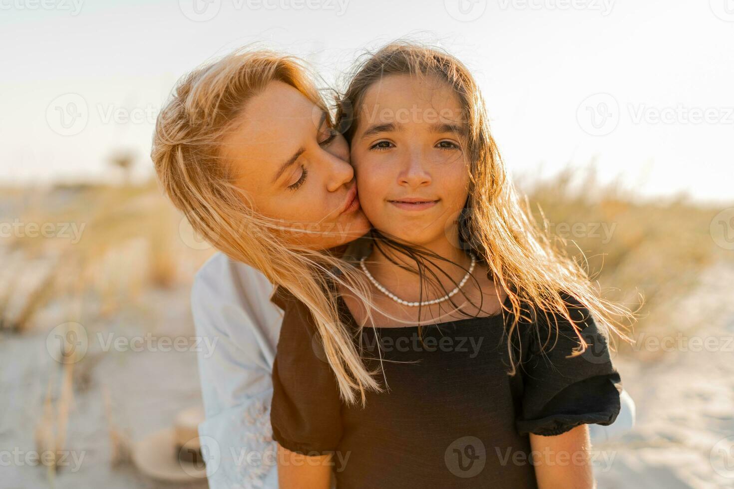 hermosa rubio madre y morena hija posando en el playa en calentar puesta de sol ligero. contento familia descansando a playa en verano. foto