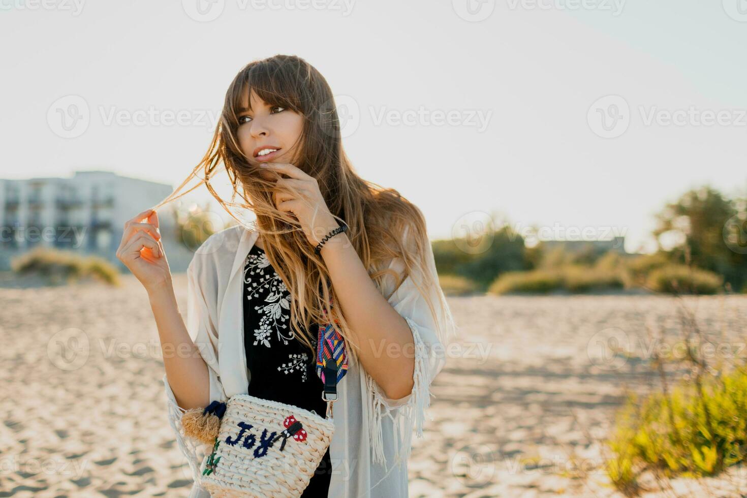 Charming girl with wavy hairs, dressed in  white boho cover up, walking on sunny summer beach. photo