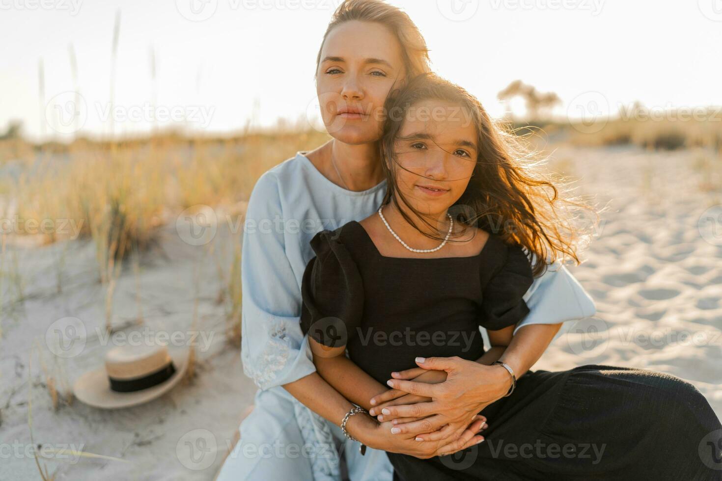 Outdoor   portrait  of beautiful family. Mother and doughter posing on the beach. Warm sunset colors. photo