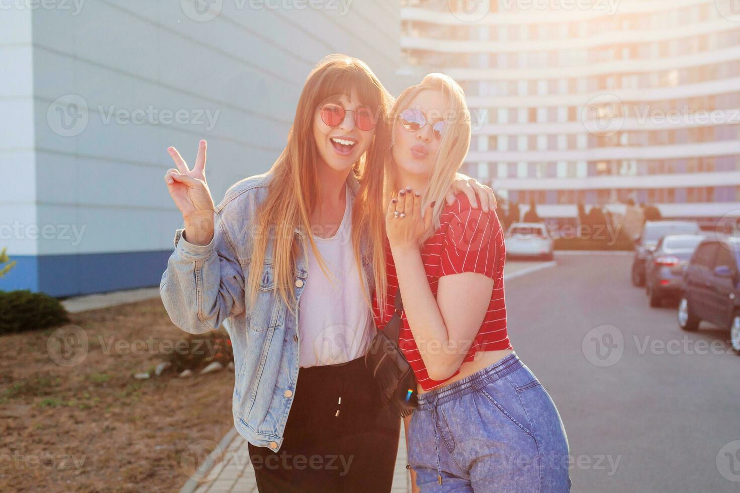 dos alegre mujer teniendo divertido exterior. elegante pantalones chaqueta con impresión. urbano antecedentes . foto