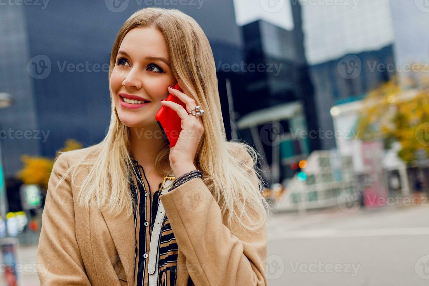 Close up portrait of smiling woman talking by mobile phone. Stylish accessories.  Beige coat. photo