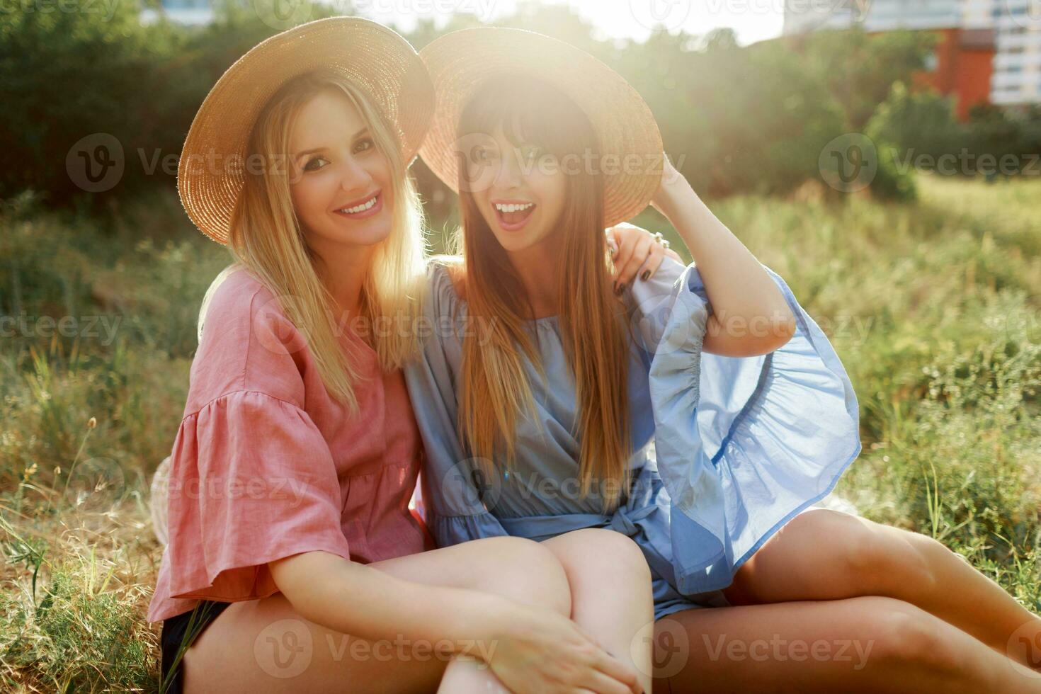 Two pretty women  in straw hat spending  holidays in countryside, drinking sparkling  wine. photo