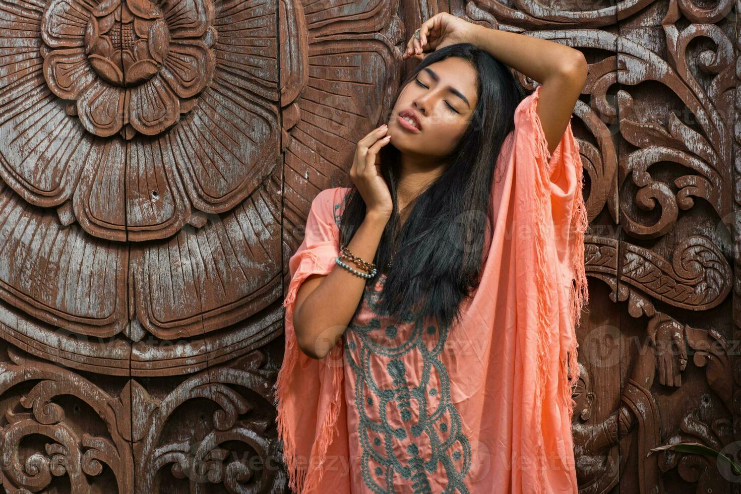 Beautiful asian model in pink boho dress posing over wood ornamental background. photo