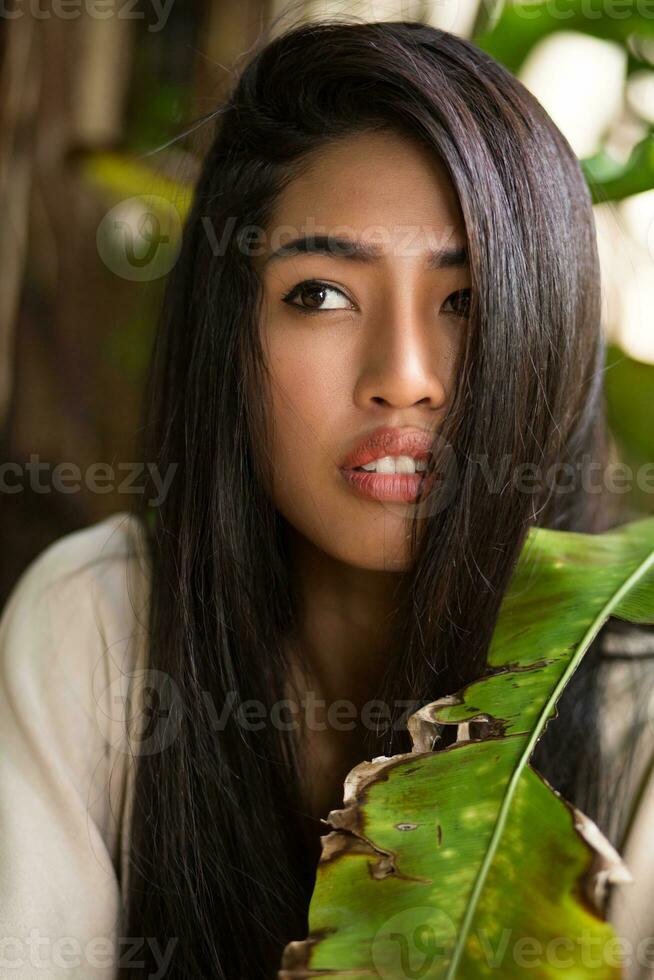 cerca arriba belleza retrato de asiático mujer con Perfecto piel posando en tropical jardín. foto