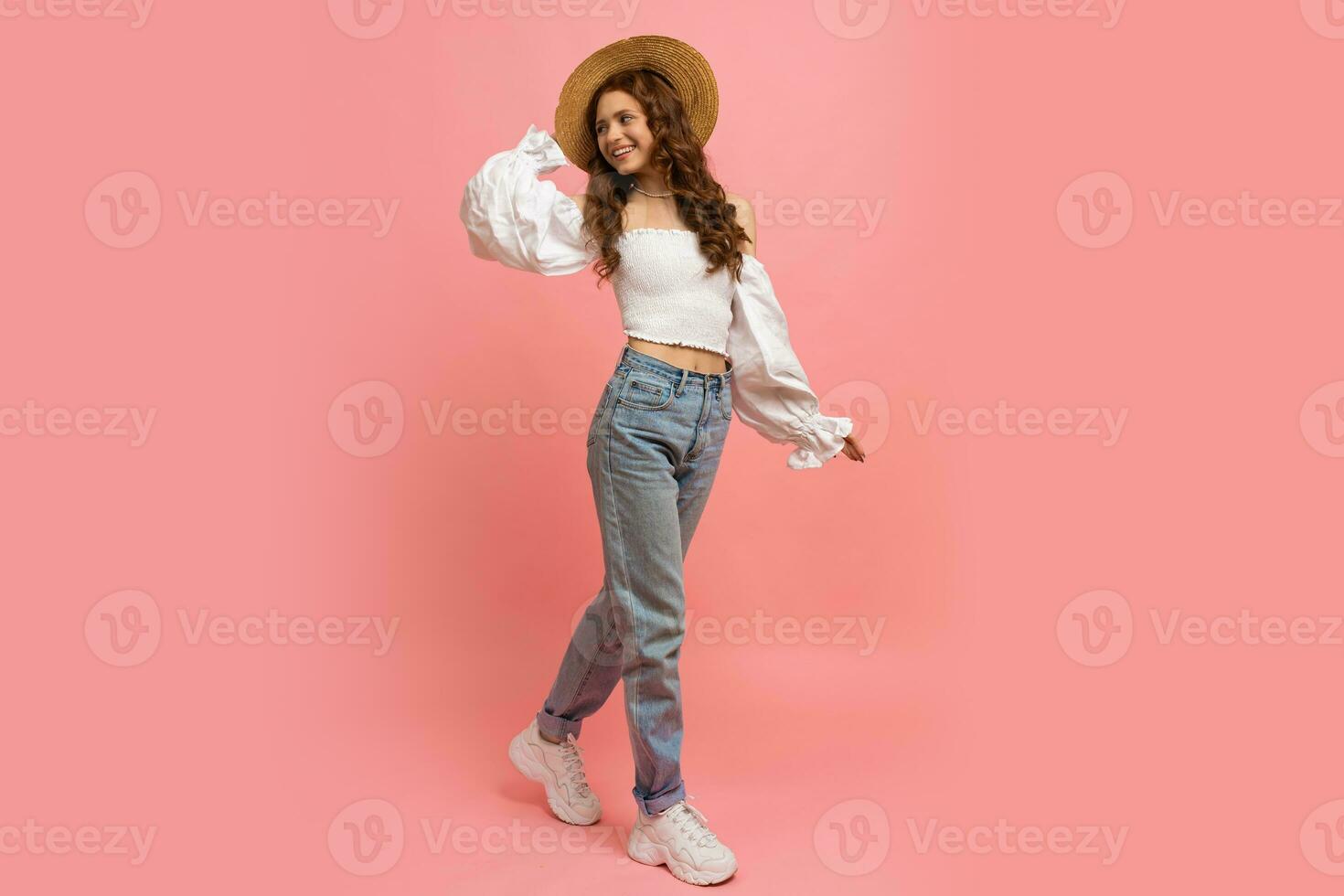 Full lenght image of Ppayful  woman in elegant linen top with balloon sleeves  and blue jeans posing on pink background.  Summer fashion trends. photo