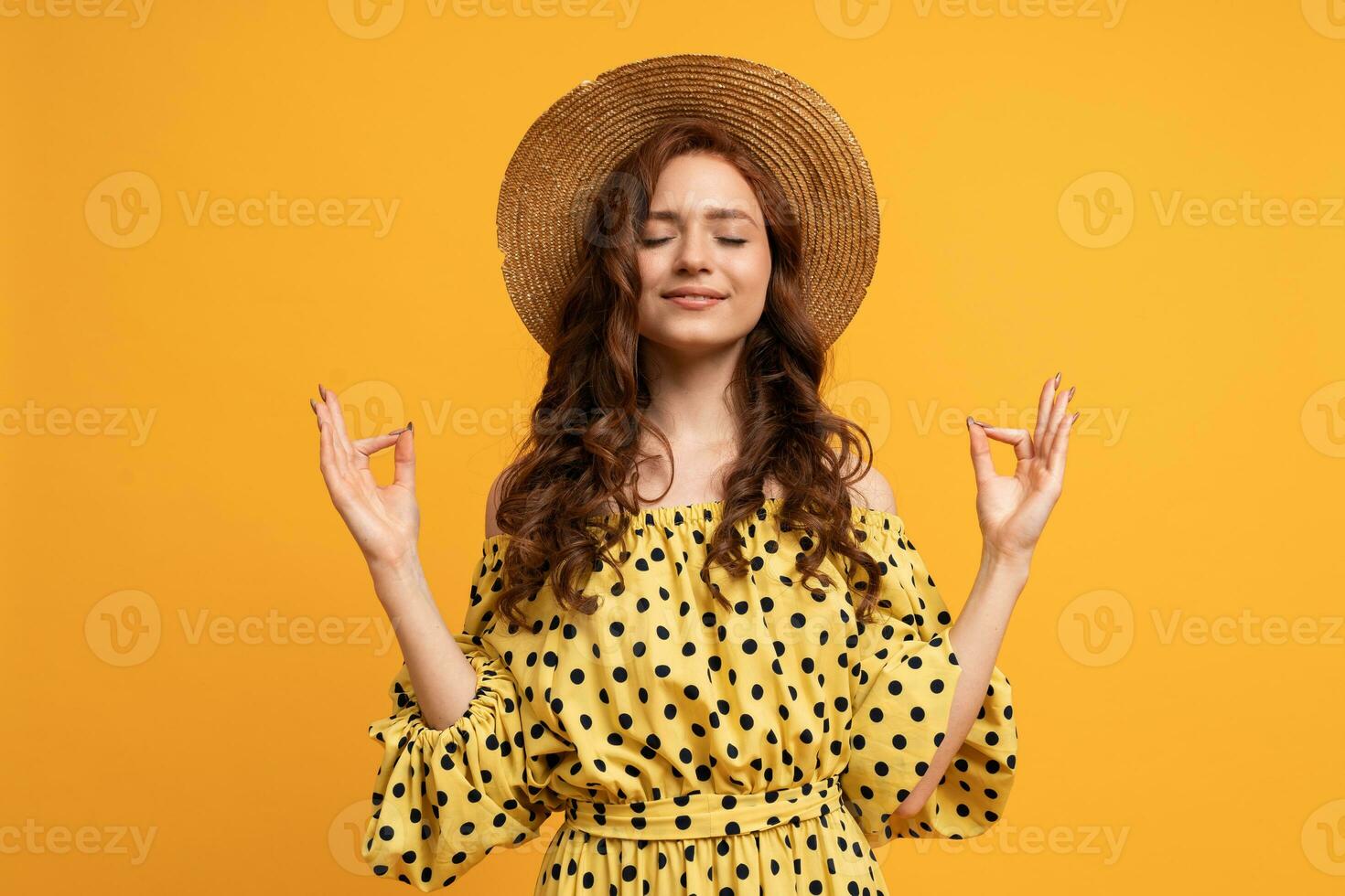 Mindful peaceful  woman meditates indoor, keeps hands in mudra gesture, has eyes closed, tries to relax after long hours of working, holds fingers in yoga sign, isolated on  yellow wall. photo