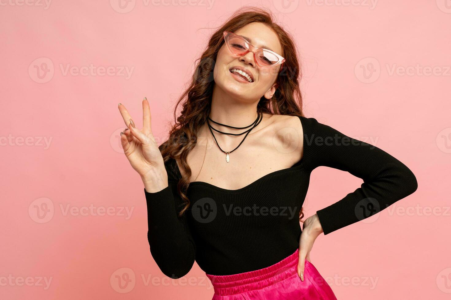 Beautiful red  head  woman  in suglasses posing over pink background. Wavy hairs. Perfect smile.  Isolate in studio. photo