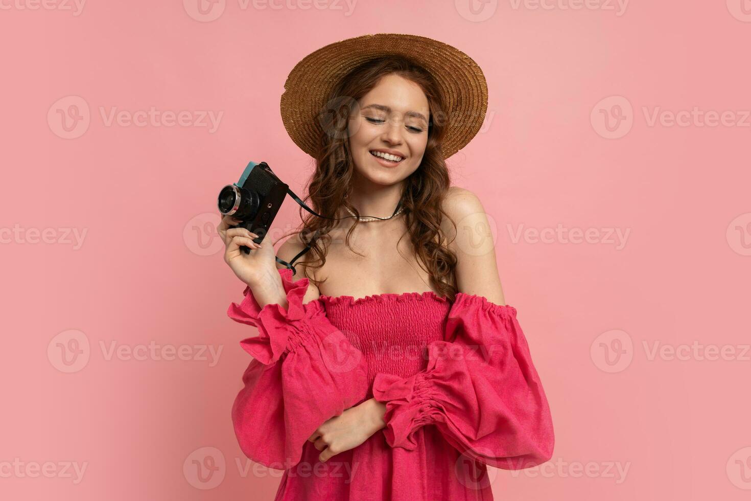 bonito rojo cabeza hembra turista con cámara. estudio Disparo de asombrado mujer participación azul retro cámara y posando terminado rosado antecedentes. foto