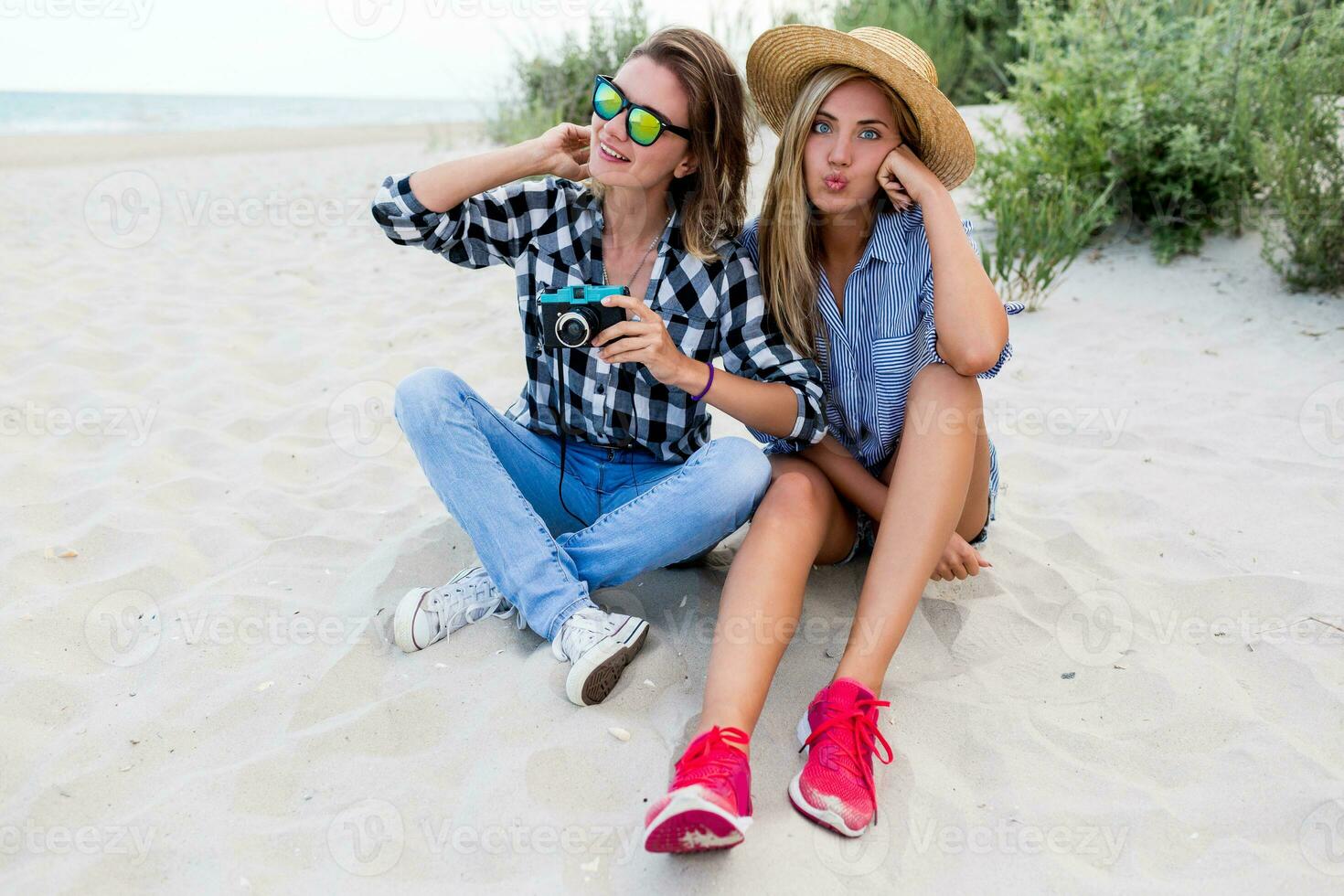 Two  women, sisters spending great time together, relaxing near ocean, making photos, laughing. photo