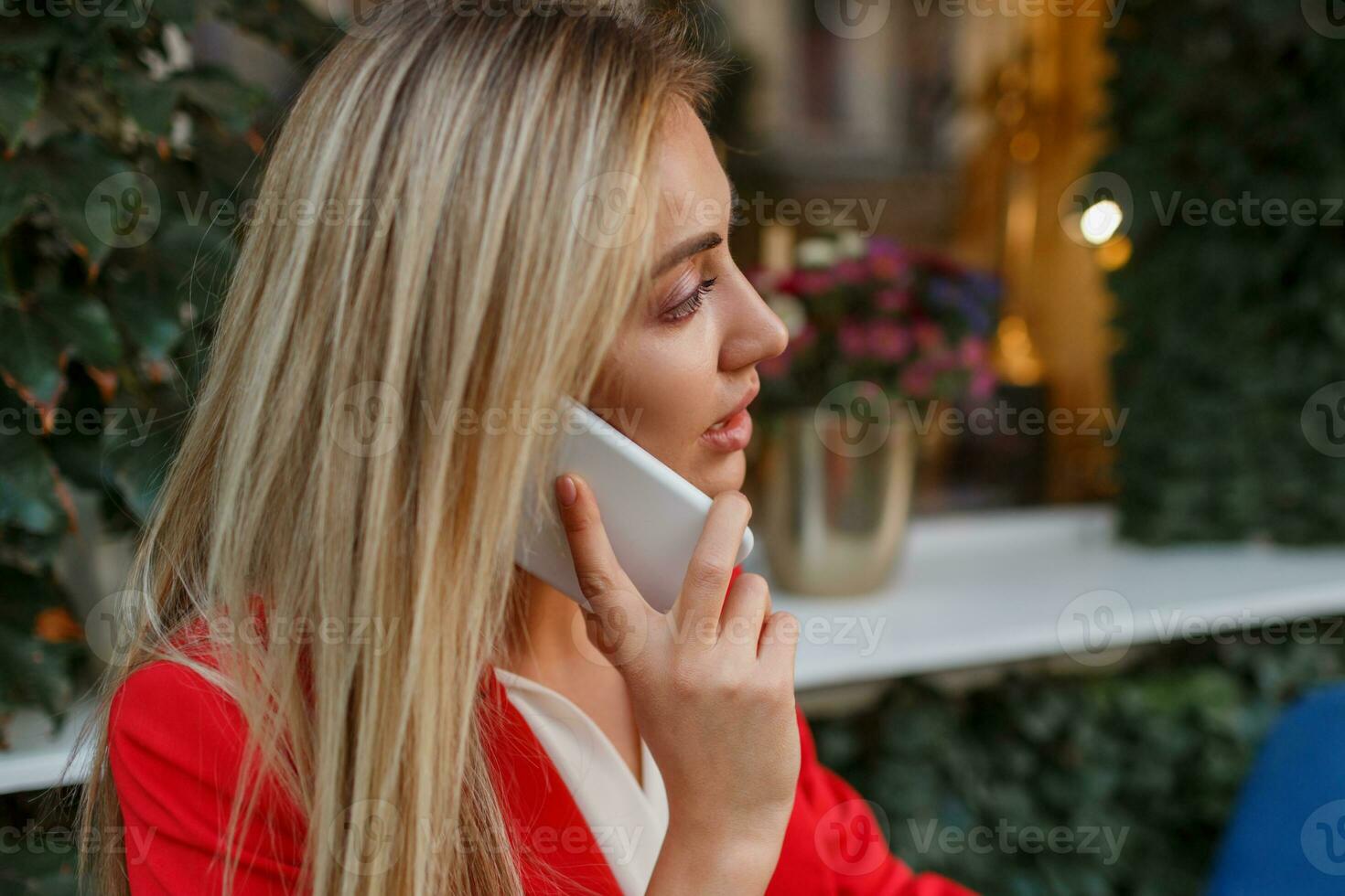 Confident  blond business woman in red stylish jacket  talking by  mobyle phone and sitting in city cafe. photo