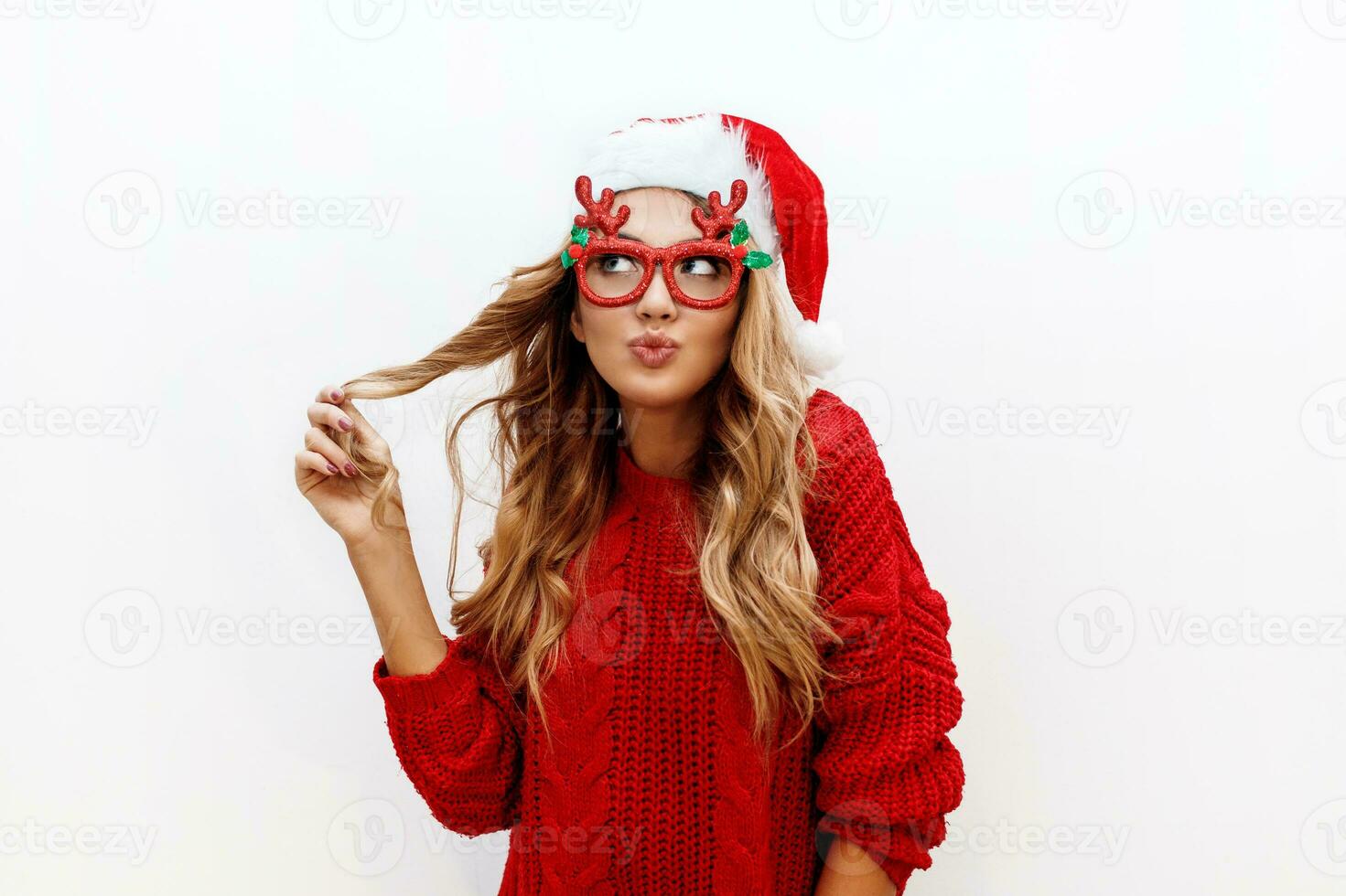alegre despreocupado rubio mujer en linda mascarada lentes y nuevo año sombrero en rojo de punto suéter posando en blanco antecedentes . aislar. Navidad y nuevo prueba fiesta concepto. foto