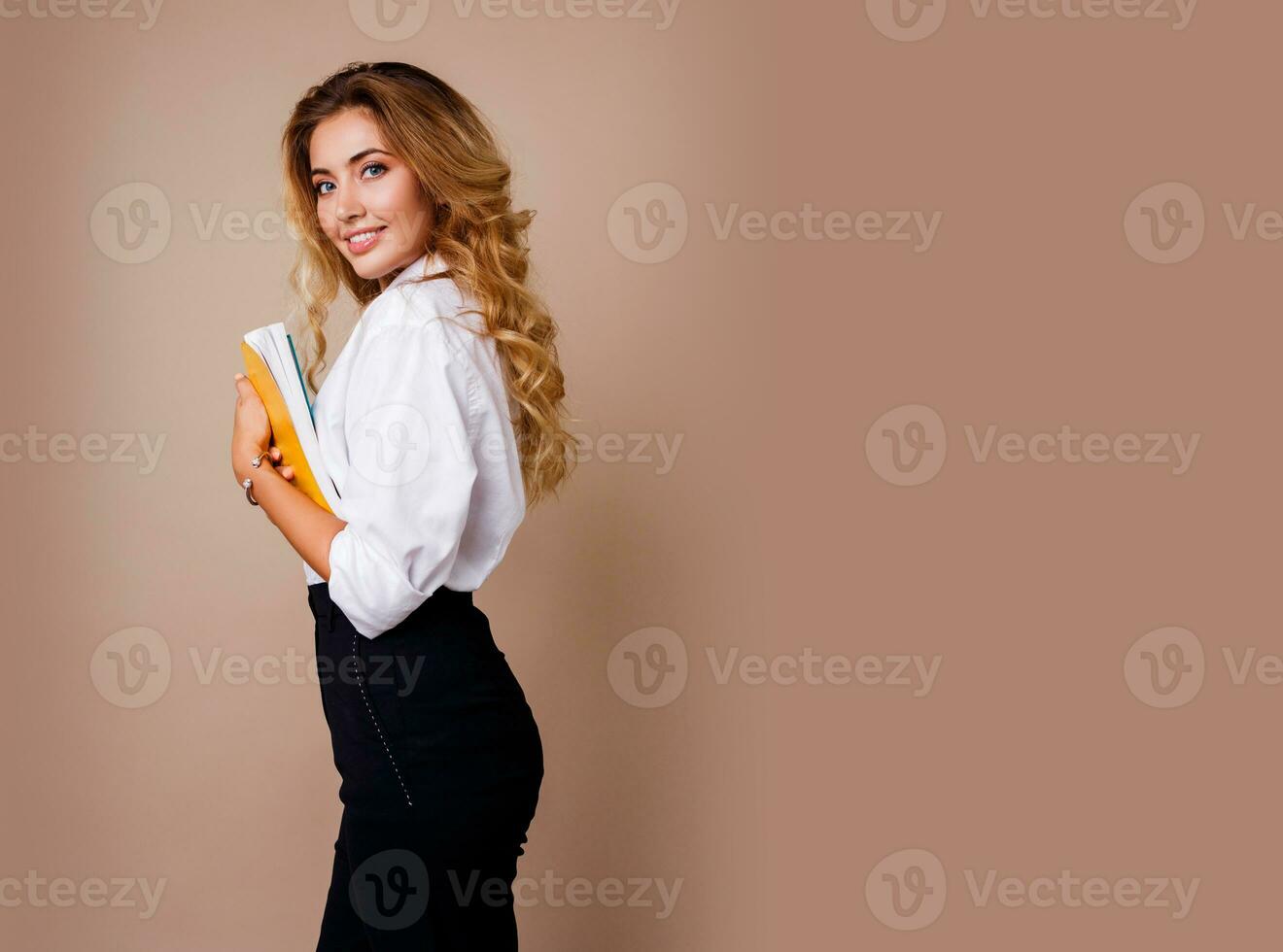 Businesswoman in stylish eyeglasses standing over beige wall. Blond wavy hairs. White blouse and  black trousers. photo