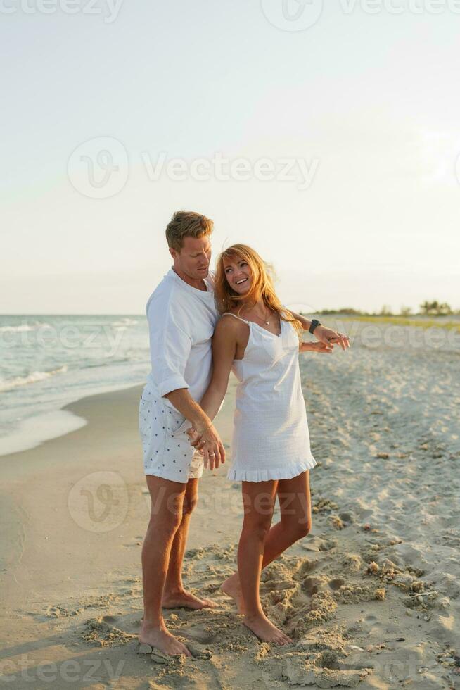 Couple in love having romantic tender moments at sunset on the beach. Wearing white clothes. Full lenght. photo