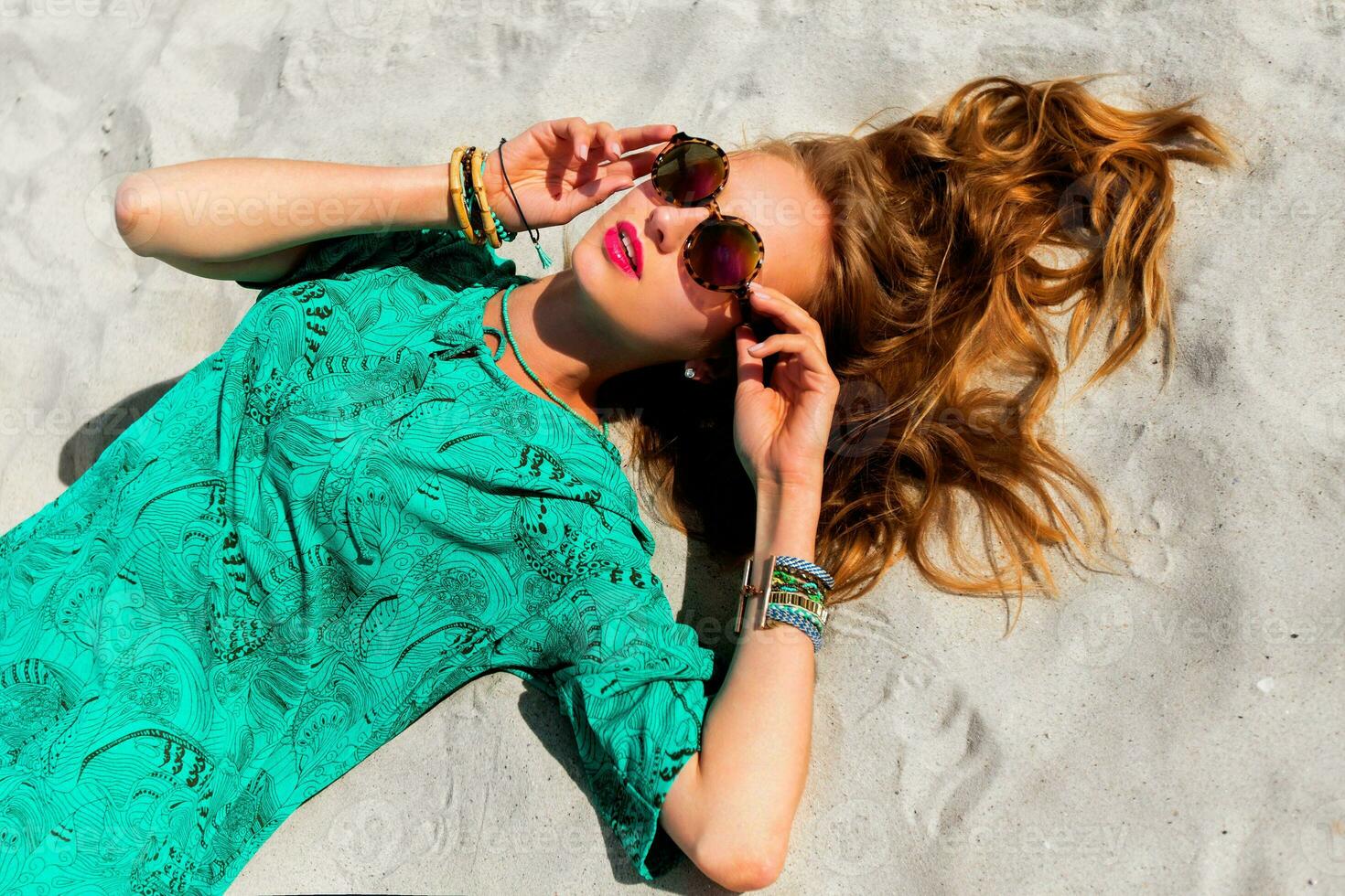 Pretty blonde girl lying on the tropical  sunny beach . Wearing cool stylish sunglasses, color    boho tunic and bright trendy accessories . Warm colors. photo