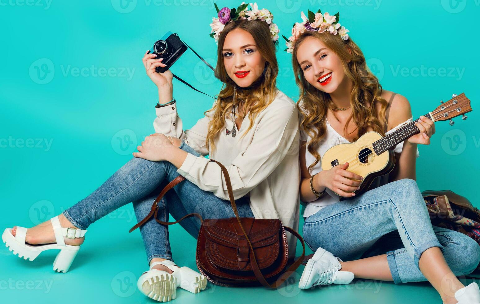 Studio lifestyle portrait of  two pretty young blonde   happy girls having fun. Making pictures in hipster style  on retro camera, wearing stylish vintage boho outfits and  flowers wreath. Spring. photo