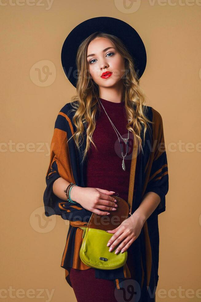 Studio close up portrait of young fresh blonde  woman in brown straw poncho , wool black trendy hat and round glasses looking at camera. Green leather had bag. photo