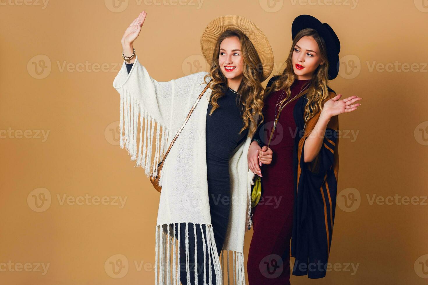 two models  with blond wavy hairstyle in wool and straw hat wearing striped poncho. American or Australian hippie bohemian style. Girls laughing  and  enjoying  time . photo