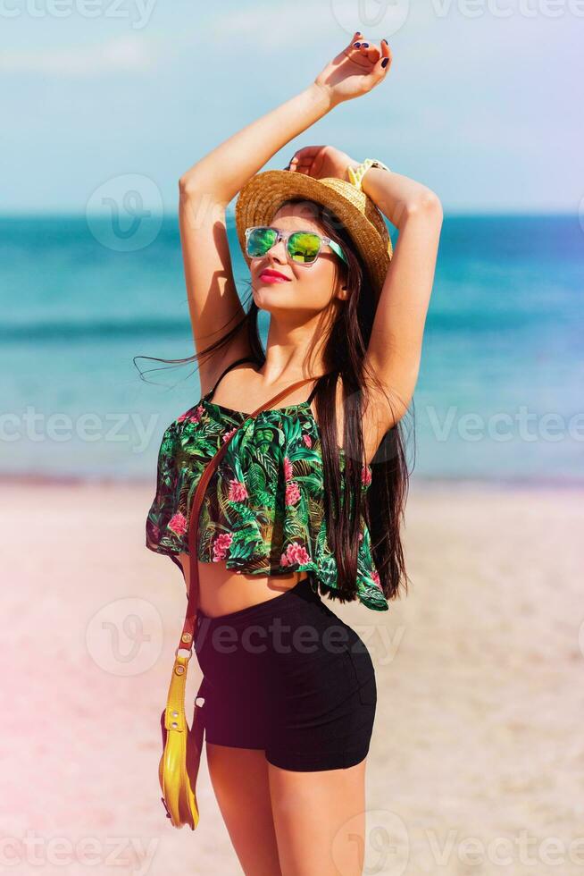 al aire libre verano estilo de vida retrato de Perfecto ajuste sonriente mujer con Perfecto cuerpo teniendo divertido en el tropical playa vistiendo Paja sombrero. brillante colores. contento humor. foto