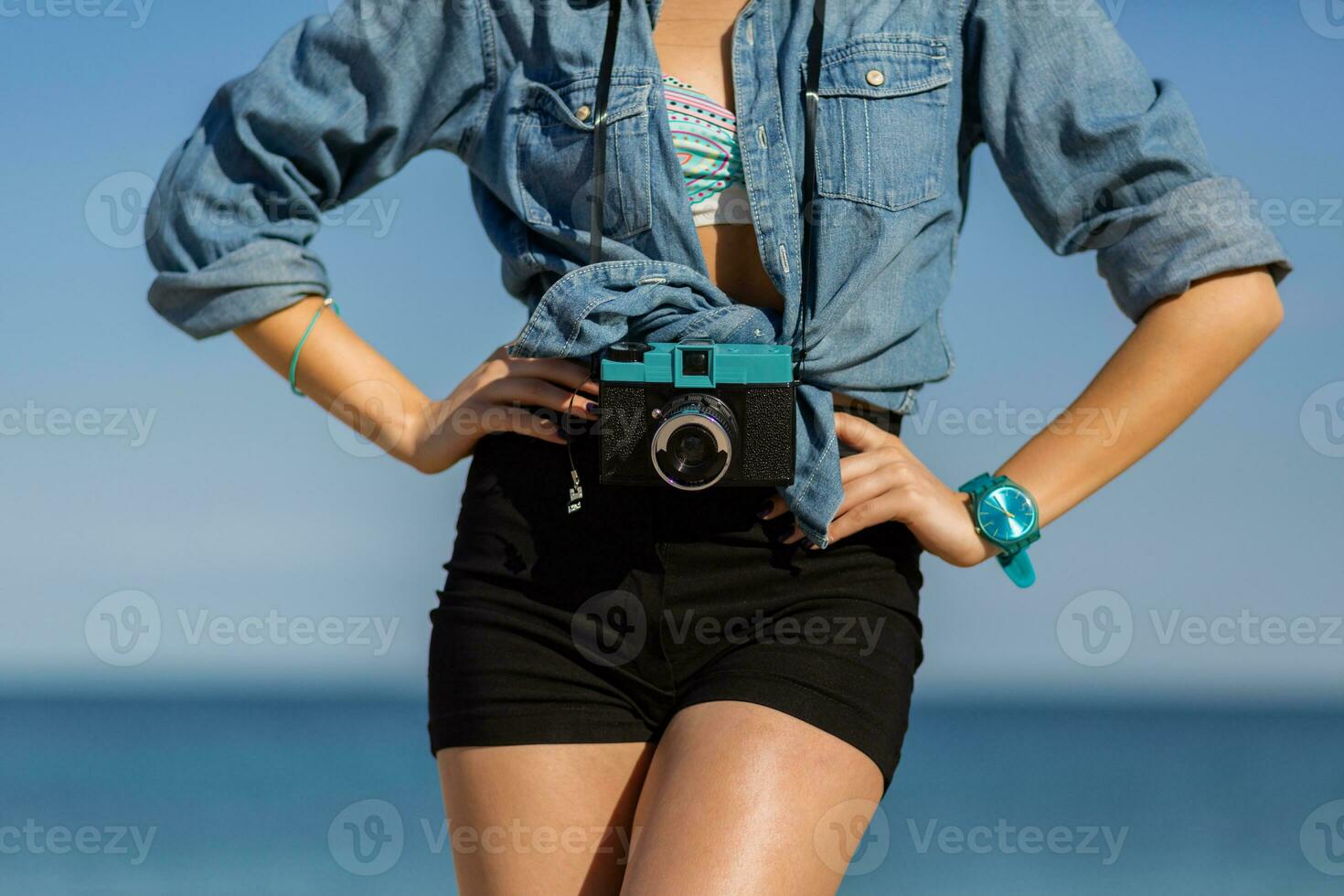 Smiling woman in straw hat and stylish  summer outfit posing with retro camera on the beach. photo