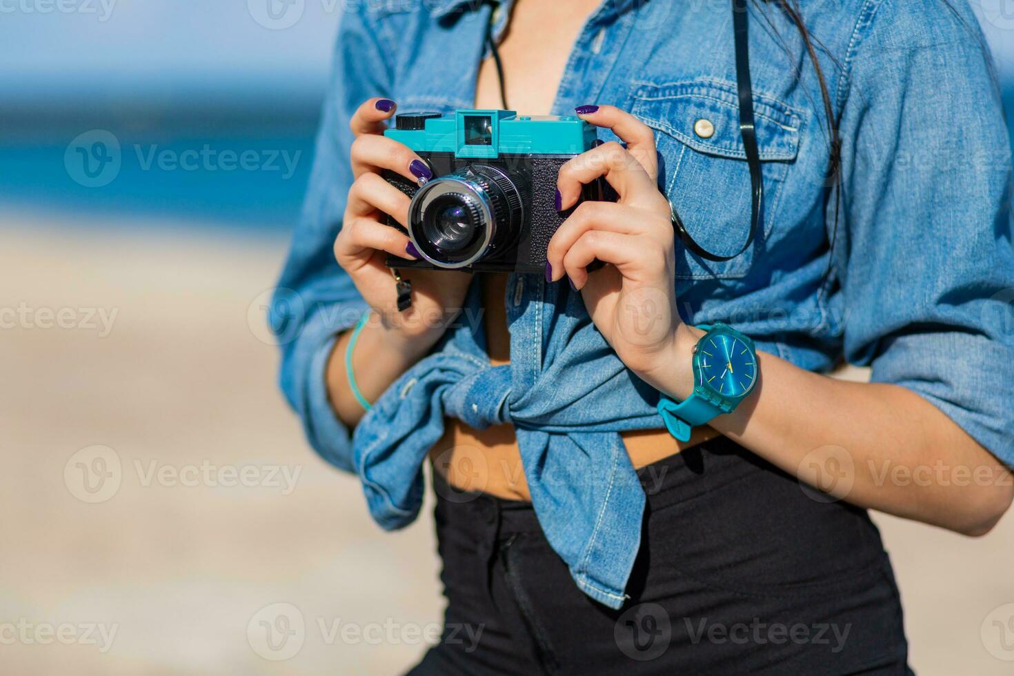 sonriente mujer en Paja sombrero y elegante verano atuendo posando con retro cámara en el playa. foto