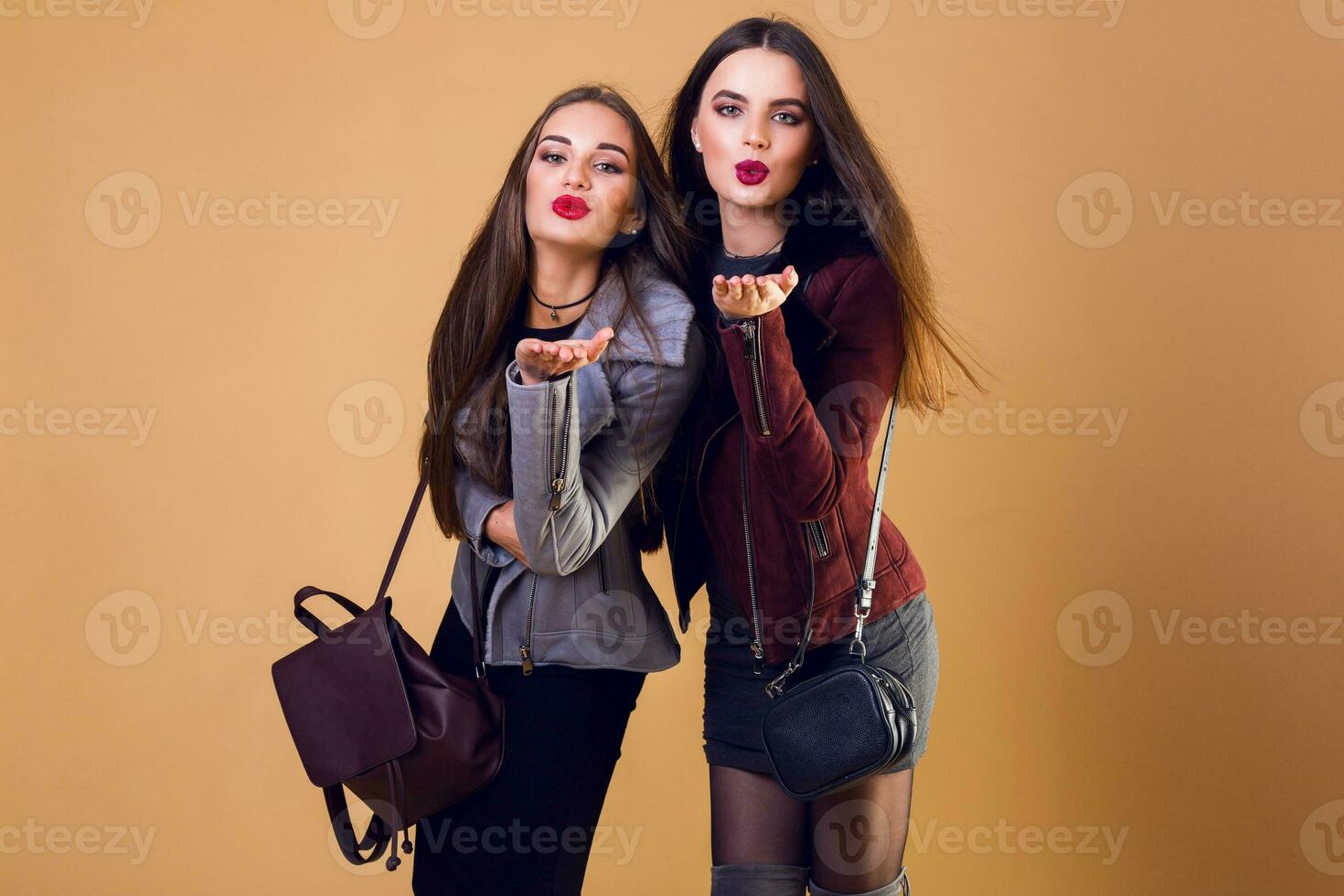 Indoor fashion portrait of two cheerful models, best friends sen kiss posing on beige or orange background . Autumn or winter c concept. Casual trendy clothes. photo