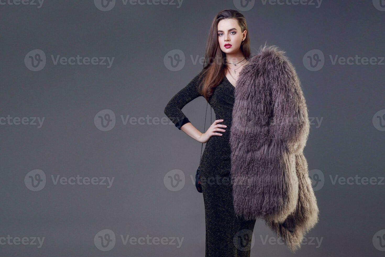 Luxury elegant woman with stylish  fur coat posing in studio , grey background.  Evening make up , red lips, brunette hairs. photo
