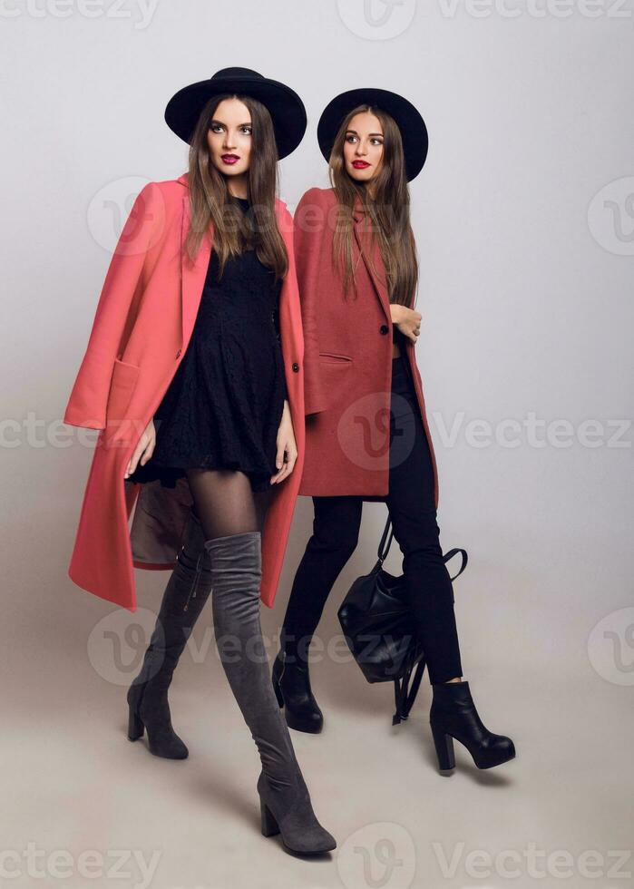 Two sisters walking. Hight fashion look.  Trendy spring clothes.  Casual models posing on grey background. Space for text. photo