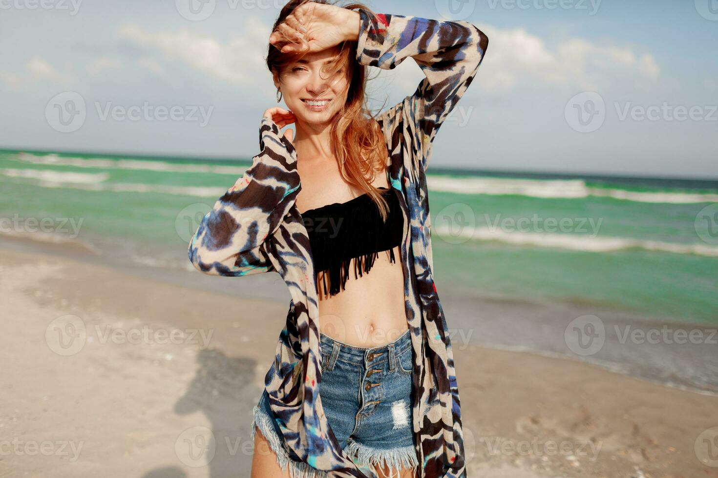 Carefree woman jumping freedom on white sand. Blue ocean background. Windy hairs. photo