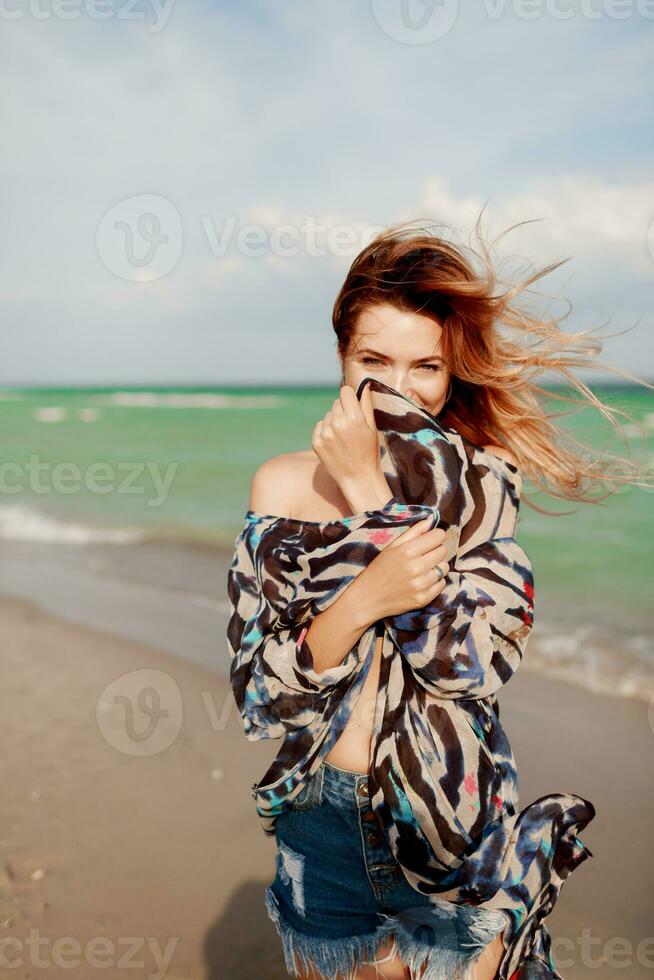 Carefree woman jumping freedom on white sand. Blue ocean background. Windy hairs. photo