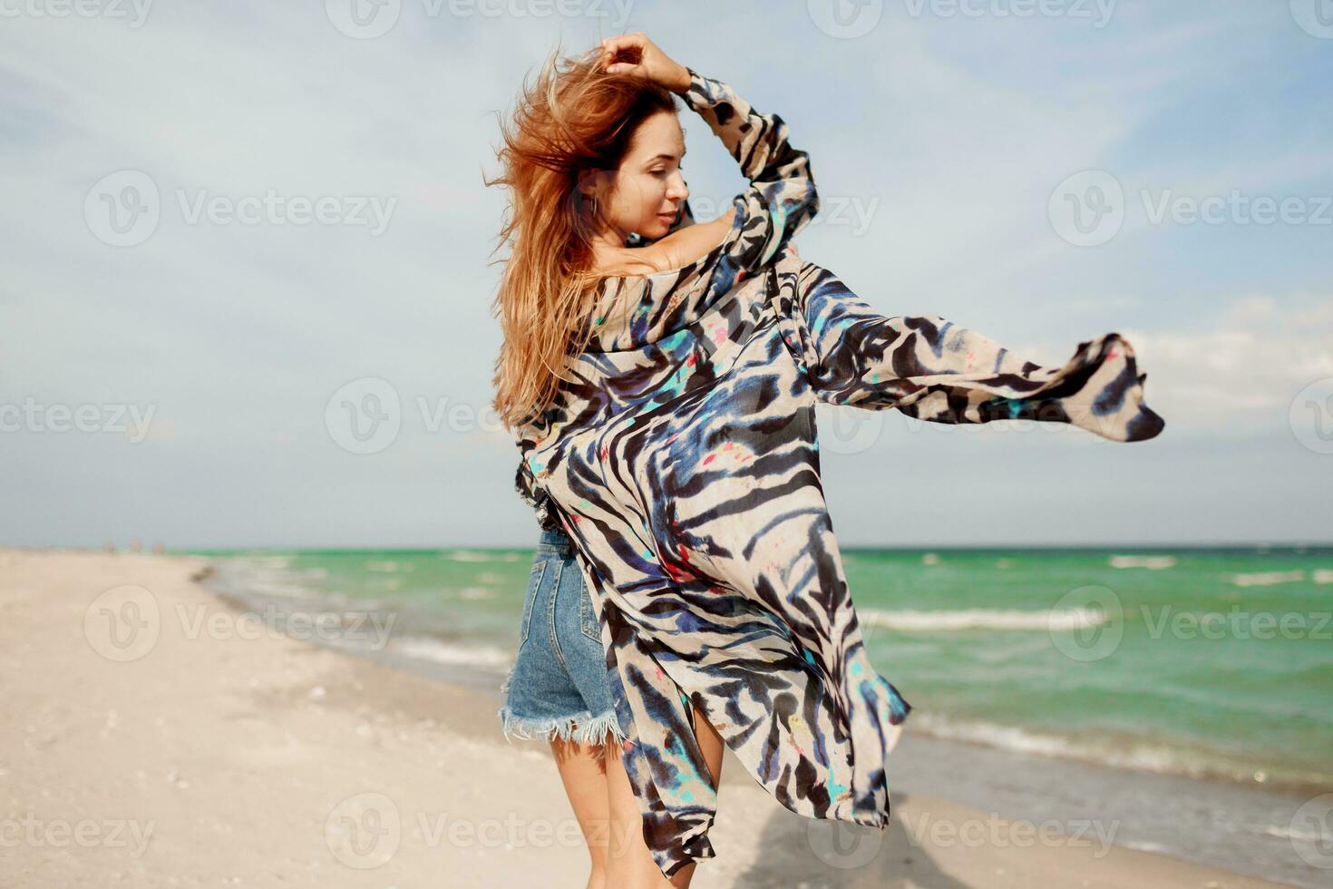 Carefree woman jumping freedom on white sand. Blue ocean background. Windy hairs. photo
