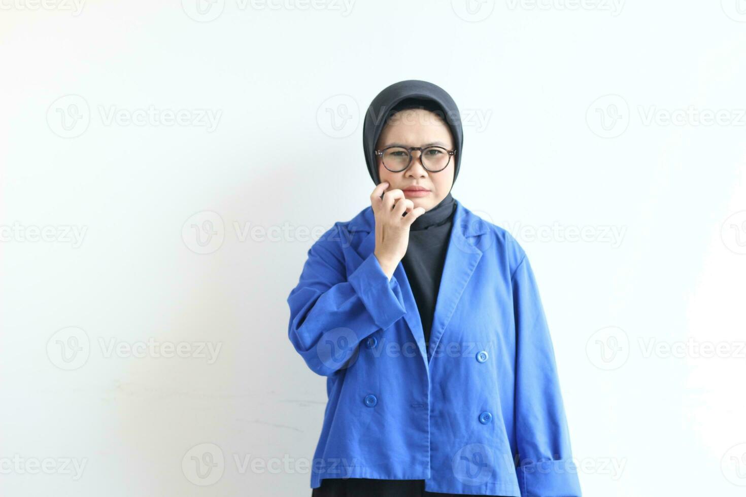 Beautiful young Asian Muslim woman, wearing glasses and blue blazer with disgusted face expression photo