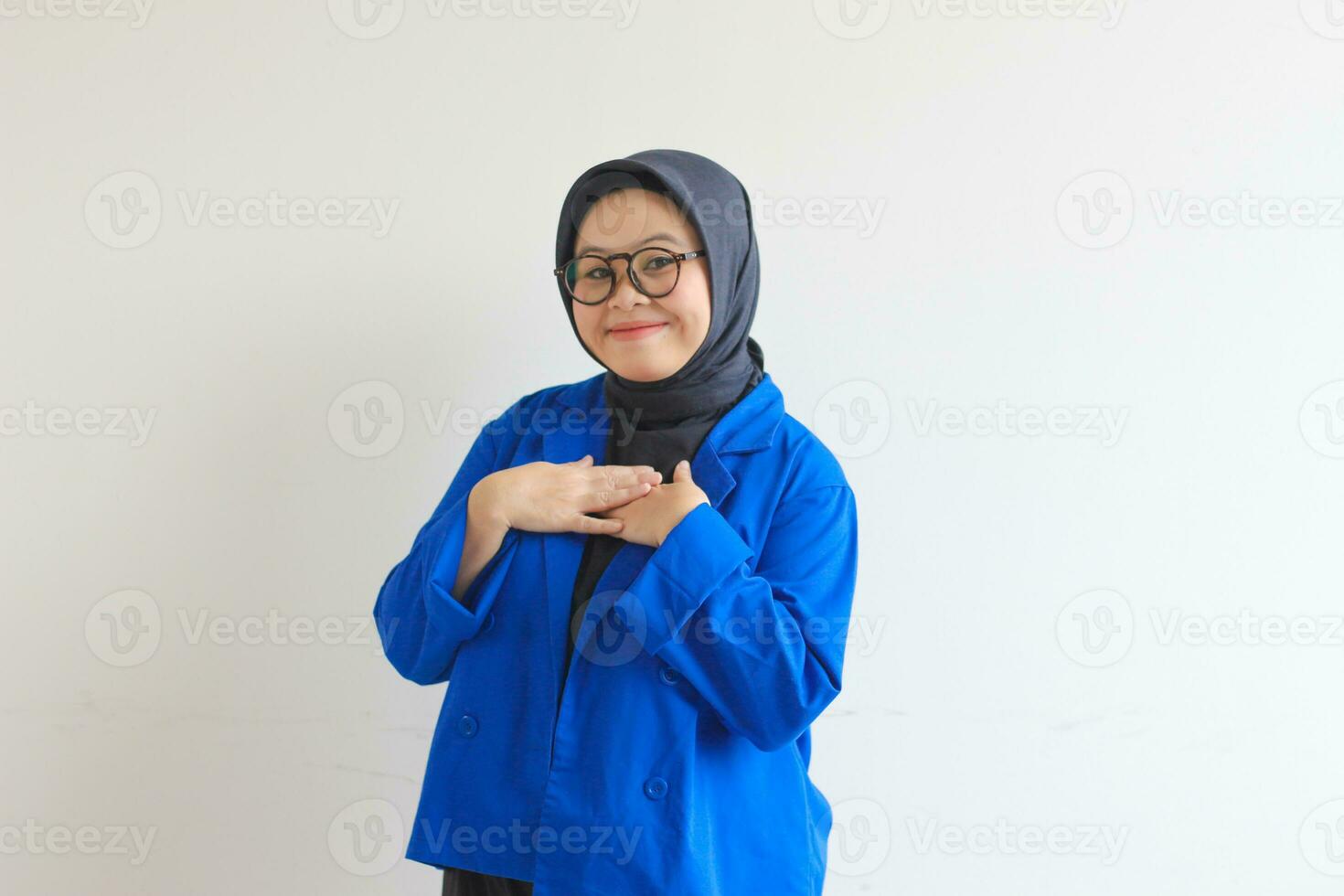 Beautiful young Asian Muslim woman in glasses and smiling putting both hands on chest and showing affection gesture photo