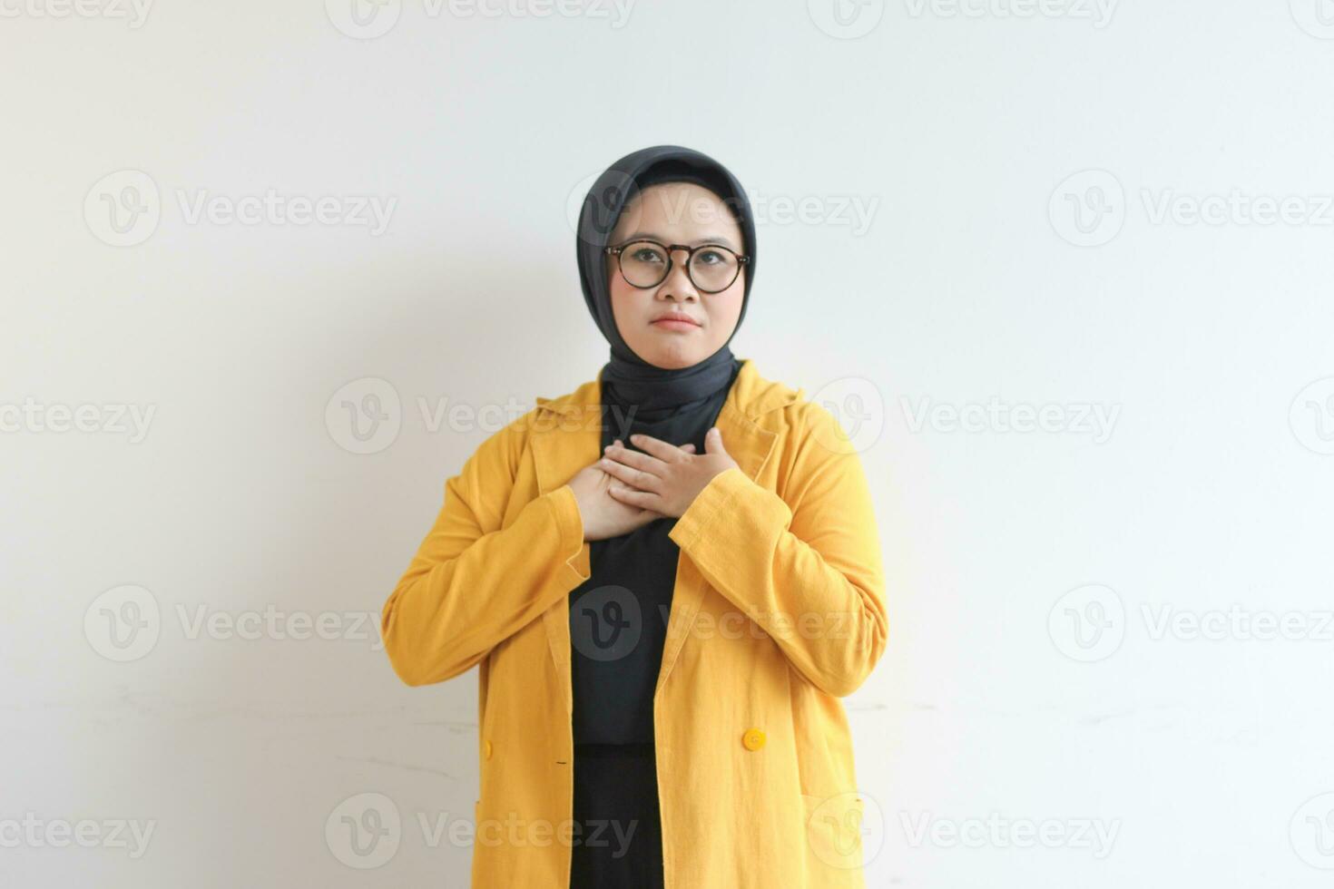 Beautiful young Asian Muslim woman in glasses and smiling putting both hands on chest with a sad expression photo