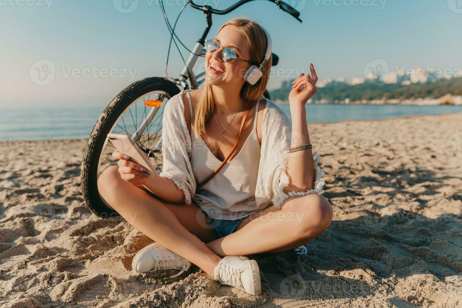 joven atractivo rubio sonriente mujer en vacaciones sentado en playa foto