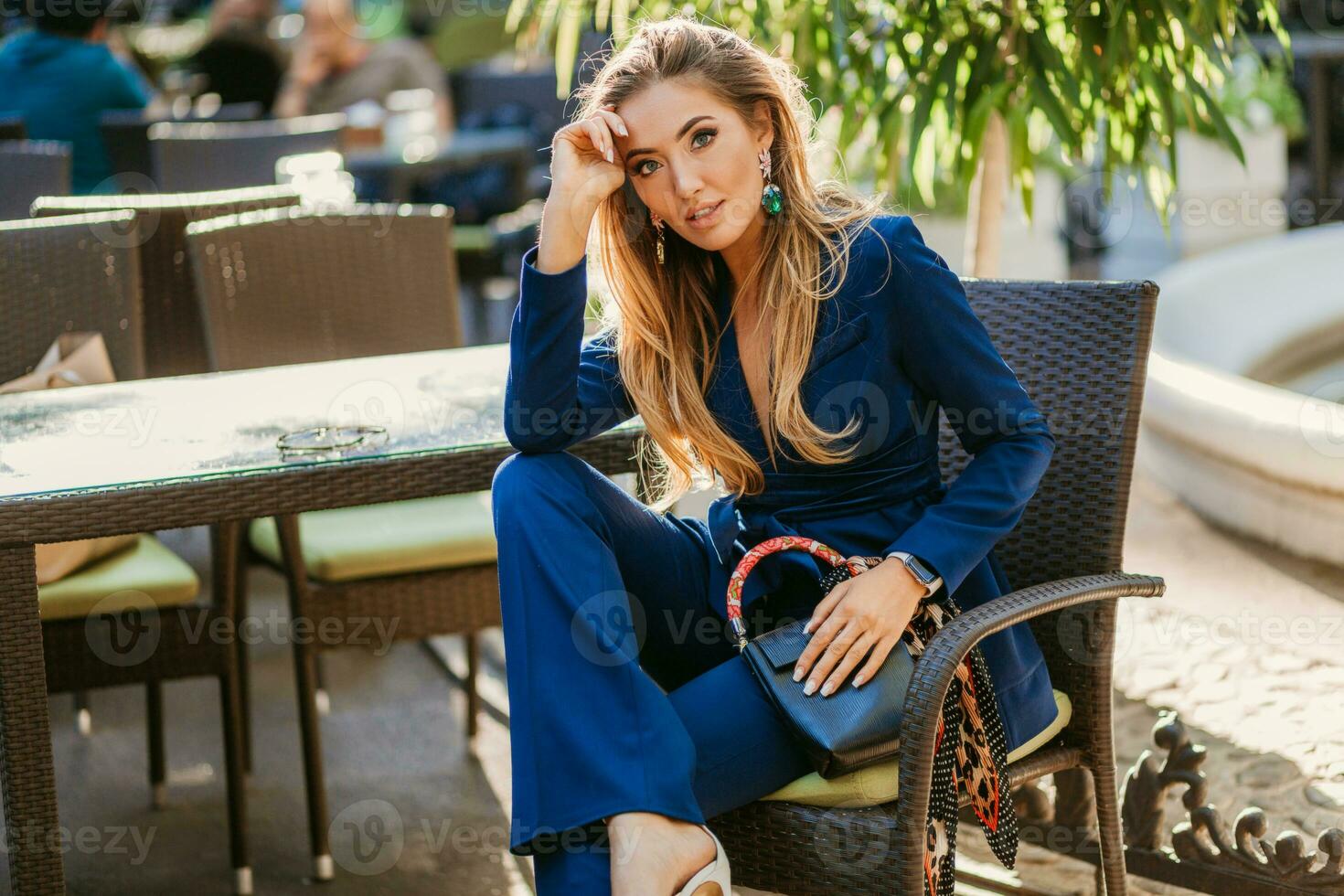 attractive woman dressed in blue elegant suit sitting in cafe in city street photo