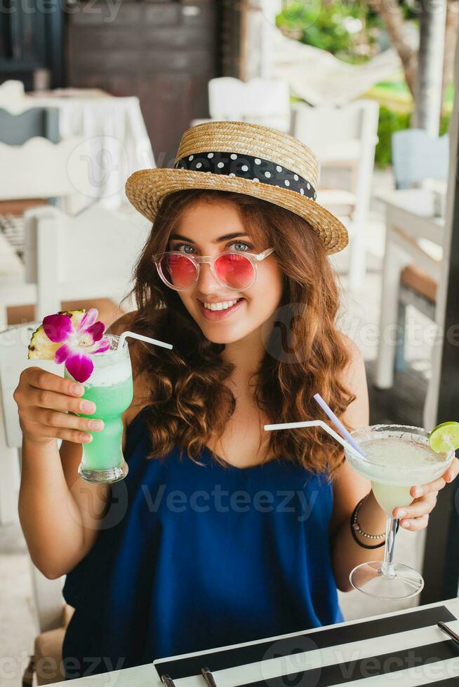 attractive young woman in blue dress and straw hat wearing pink sunglasses drinking cocktails photo